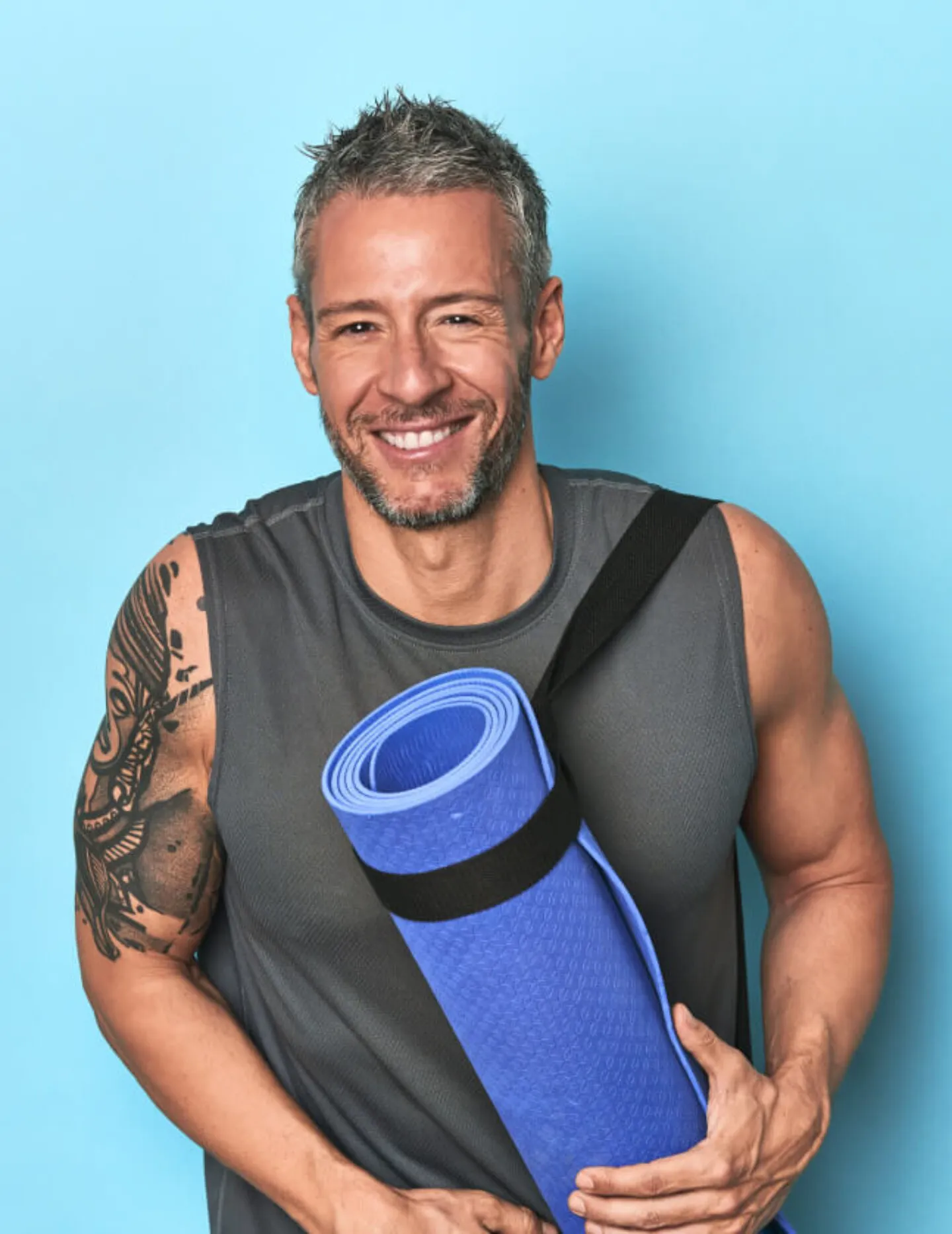 Uśmiechnięty mężczyzna trzyma matę, jest przygotowany do treningu fitness na siłowni Total Active Krosno